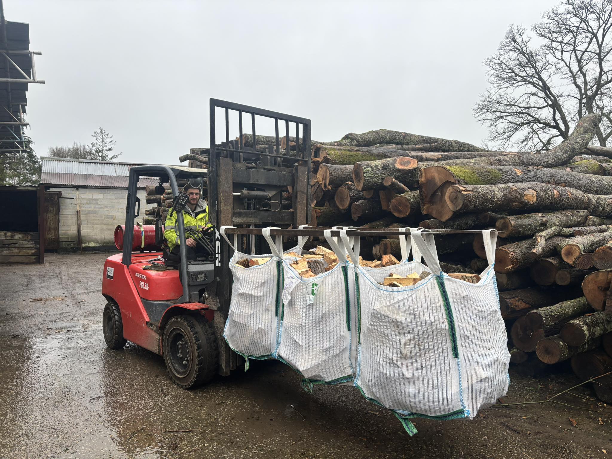 Forklift carrying tonne bags of logs past a stack of raw timber