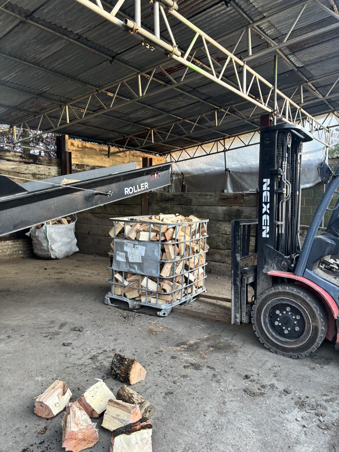 A roller conveyor and forklift moving a crate of split logs through the barn